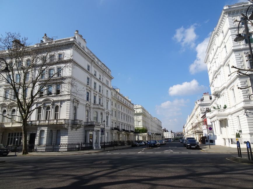 A row of historic sandstone residential buildings with large sash windows and decorative cornices line a street in St Johns Wood Abbey Road. The cobblestone sidewalk runs alongside the buildings, with